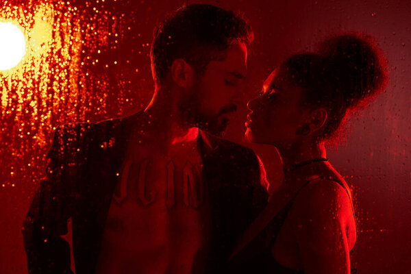 Пара разделяет нежный момент, освещенный теплым светом, окруженный каплями дождя на стекле.