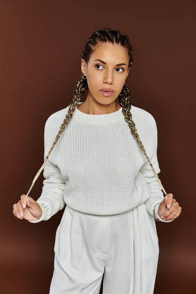 A stylish young woman stands confidently, wearing autumn inspired attire with elegant braids.