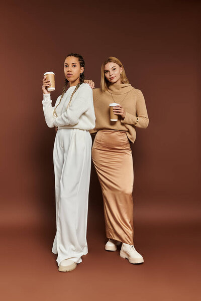 A charming couple dressed in cozy autumn outfits stands together, holding warm beverages.