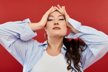 Göz kamaştırıcı makyajlı, genç ve iri bir kadın ellerini başının üstüne koyup, güzel bir poz veriyor..