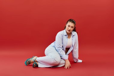 Bright makeup enhances the beauty of a young plus size woman as she poses against a striking red background. clipart