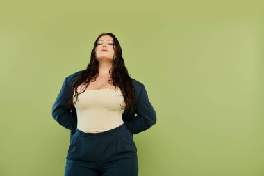 Kıvırcık saçlı çarpıcı ve iri yarı bir kadın canlı yeşil bir arka plana karşı şık bir takım elbiseyle poz veriyor..