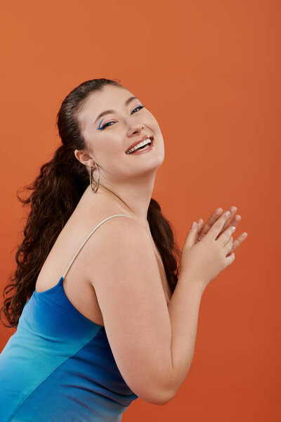 Красивая женщина плюс размер улыбается ярко, одетый в синее платье, в красочной обстановке студии.