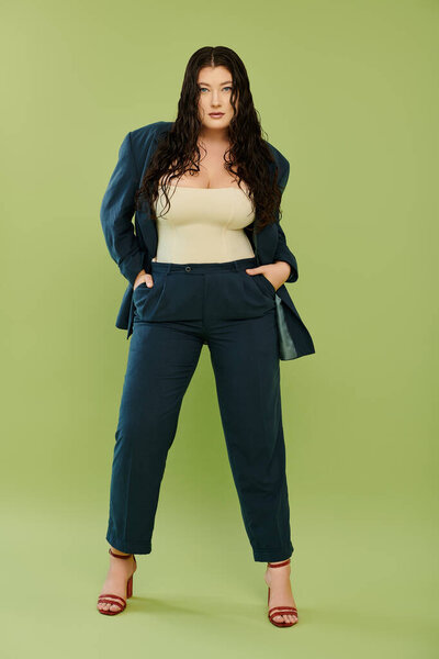 A young, beautiful plus size woman showcases her style in a fitted suit, exuding confidence on a green backdrop.