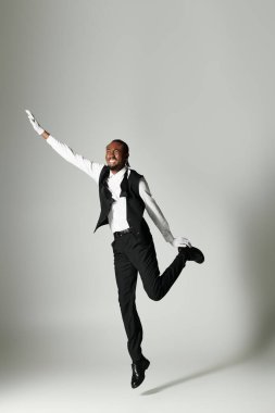 A young man exudes confidence in a sharp suit, showcasing a lively jump with a vibrant smile from a grey background. clipart