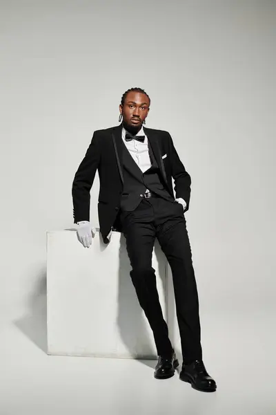 stock image A confident young man in a tailored suit and vest stands elegantly on a grey background, showcasing his style.