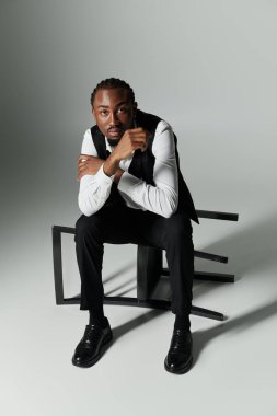 Takım elbiseli genç bir Afrikalı Amerikalı. Gri bir arka plana karşı eşsiz bir sandalyede otururken kendine güveni tam..