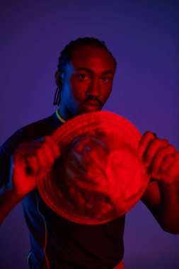 Genç bir adam, elinde eşsiz bir şapkayla parlayan neon ışıklarına karşı moda anlayışını sergiliyor..