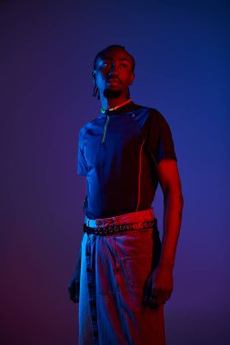 Genç bir Afrikalı Amerikalı, stüdyodaki neon ışıklarla aydınlatılan şık kıyafetlerini sergiliyor..