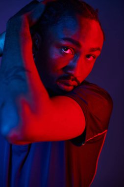 Genç bir Afrikalı Amerikalı, neon ışıklı bir stüdyoda dinamik bir poz verirken şık kıyafetini sergiliyor..