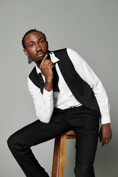 A confident young Black man in a sleek suit poses against a neutral grey background.