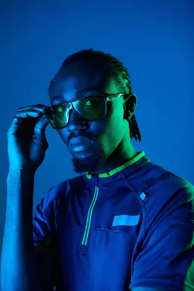 stock image A young man showcases his fashion sense, donning stylish attire and striking a pose amidst vibrant neon lights.