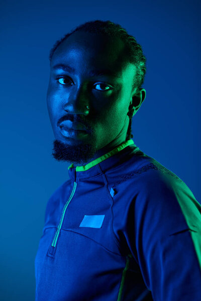 A young man showcases his fashion sense in a trendy outfit, illuminated by striking neon hues in a studio.