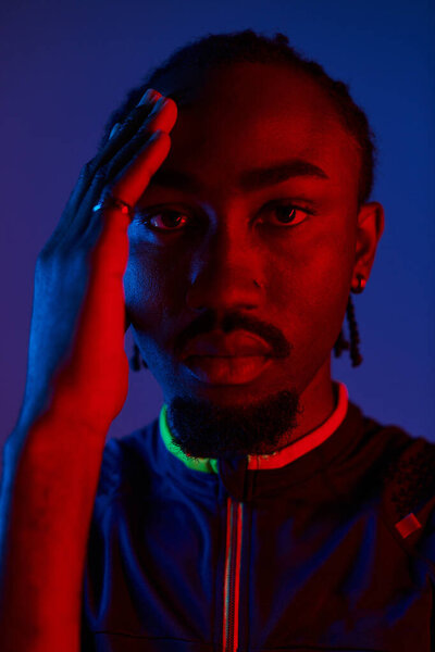 Молодой афроамериканец в модном наряде уверенно позирует с неоновыми огнями, придающими яркие тона..