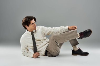 Şık giyinmiş genç bir adam, kendine güvenen bir duruş sergiliyor. Stüdyoda cazibe ve entelektüellik yayıyor..