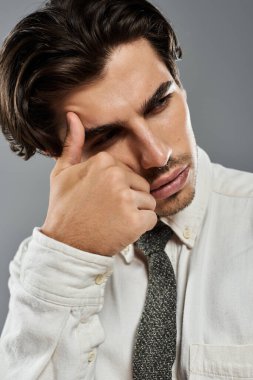 Genç, yakışıklı bir adam, minimalist gri bir arkaplan karşısında zarif bir şekilde poz verir..
