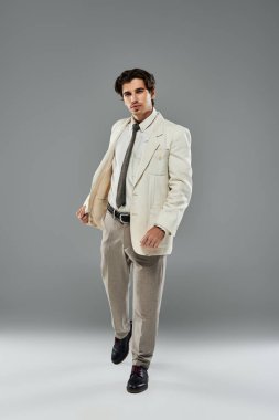Genç ve yakışıklı bir adam cazibesini gösterip şık resmi kıyafetler giyer ve stüdyo ortamında kendine güveni tamdır..