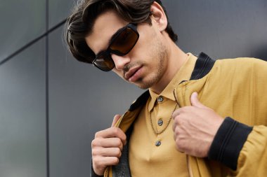 Kendine güvenen genç bir adam modern bir şehir manzarasına karşı poz verirken modaya uygun sonbahar kıyafetini sergiliyor..