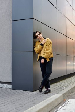 Modayı takip eden genç bir adam, çağdaş bir yapının moda bir sonbahar elbisesine güvenerek poz veriyor..