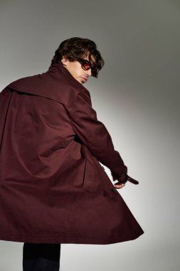 Moda bir sonbahar kıyafeti giyen genç bir adam, minimalist bir arkaplana karşı güvenle poz veriyor..