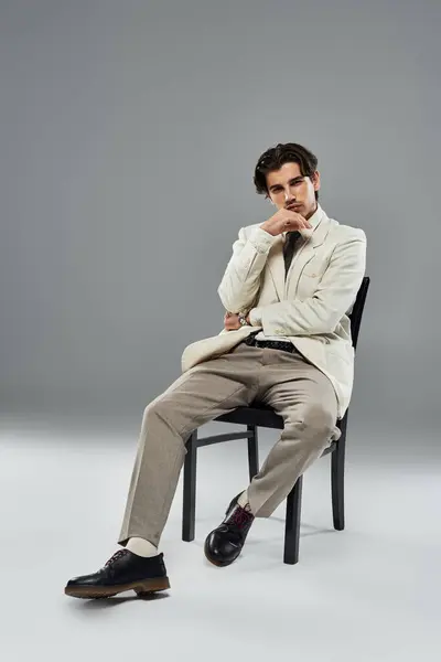 stock image A young man showcases confidence in stylish formal wear as he poses thoughtfully against a grey backdrop.