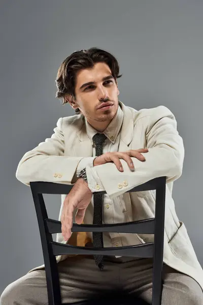 stock image A young man dressed impeccably in a formal outfit leans on a chair, exuding charm and elegance.