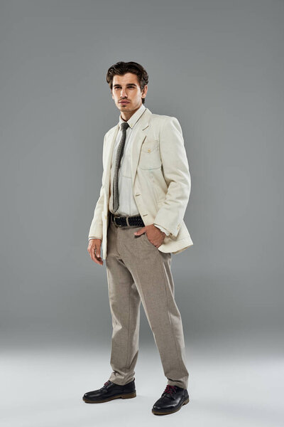 Молодой, красивый мужчина элегантно стоит в формальной одежде, излучая уверенность в обстановке студии.
