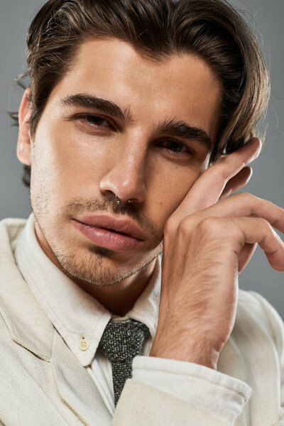 A stylish young man stands confidently in formal wear, showcasing a modern look against a grey setting.