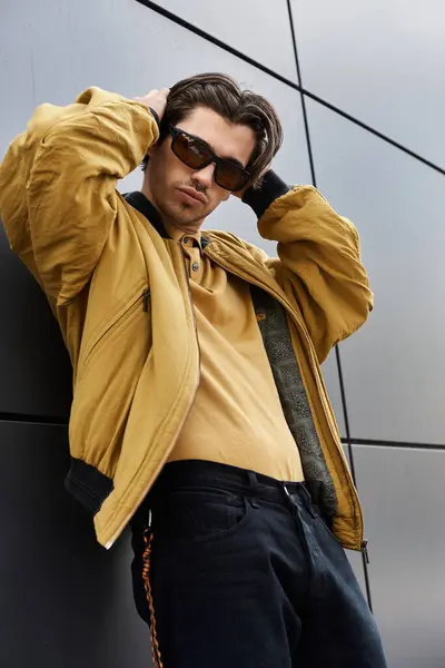 Stock image A young man showcases his trendy autumn outfit while leaning casually against a sleek building.