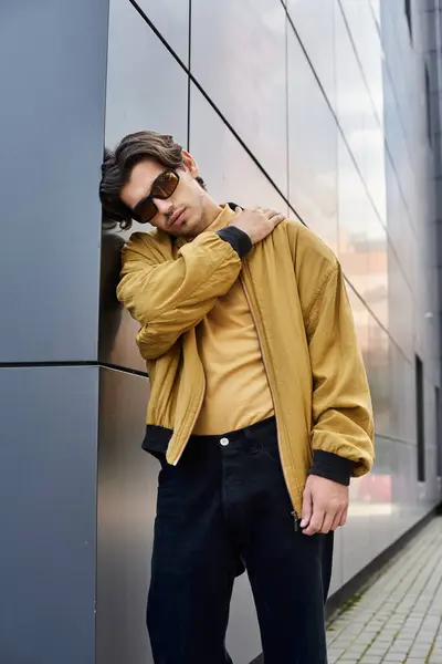 stock image The young man leans casually against a modern building, exuding confidence in his trendy autumn attire.