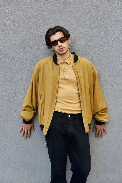 stock image A young man showcases his fashionable autumn outfit while leaning casually against a gray wall.