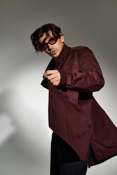 Молодой человек уверенно позирует в модном осеннем наряде, демонстрируя свой уникальный стиль при мягком освещении.