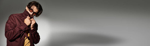 Молодой человек уверенно позирует в осеннем наряде, подчеркивая свой модный стиль на нейтральном фоне.