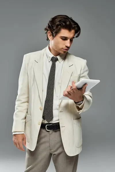 stock image A young man dressed in fashionable formal wear interacts with a tablet, showcasing confidence and style.