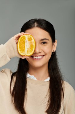 A young woman with long hair playfully covers one eye with an orange, radiating joy. clipart