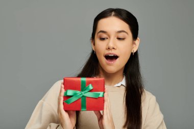 Heyecanlı bir yüzü olan genç bir kadın güzel paketlenmiş bir hediye tutuyor ve tarzını gösteriyor..