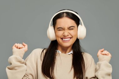 A young woman joyfully expresses her love for music while wearing headphones indoors. clipart