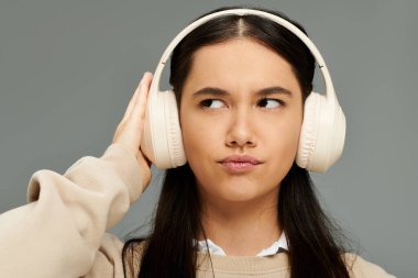 Şık kıyafetler giyen genç bir kadın kulaklıkla düşünceli bir şekilde müzik dinliyor..