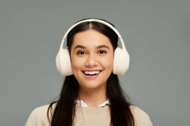 Kulaklıklı genç bir kadın, neşeli bir şekilde gülümseyerek, samimi bir mekanda müzik eşliğinde mutluluğunu ifade ediyor..