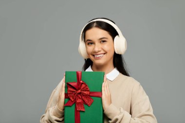 A stylish young woman radiates joy while presenting a wrapped gift box adorned with a red bow. clipart