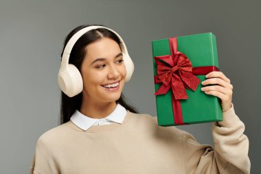 Moda elbiseli genç bir kadın elinde kurdeleyle süslenmiş bir hediyeyle gülümsüyor..
