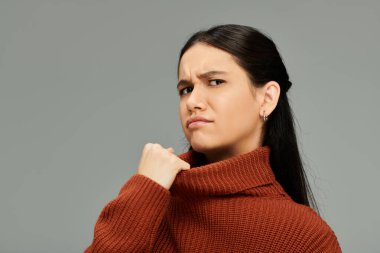 Paslı kazak giyen genç bir kadın minimalist bir ortamda büyüleyici bir duygusal ifade sergiliyor..