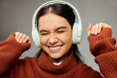 Genç bir kadın kulaklıkla müzik dinliyor, gülümseyerek duygularını neşeyle ifade ediyor..