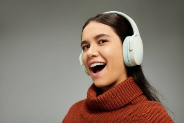 Şık bir tarzı olan genç bir kadın kulaklıkla müzik dinlerken neşe ifade ediyor..
