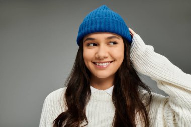 A young woman expresses happiness and style, wearing a cozy sweater and bright blue beanie. clipart