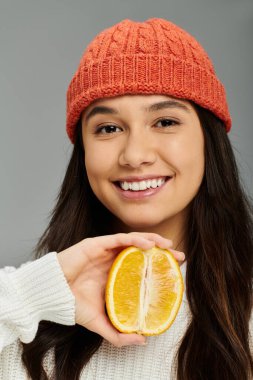 A cheerful young woman smiles warmly while holding a halved orange near her face. clipart