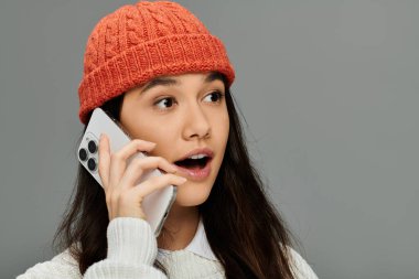 Samimi bir şapka takan şık genç bir kadın telefon görüşmesi sırasında heyecanla tepki veriyor..