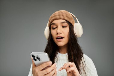 A stylish young woman expresses emotions as she engages with her phone, enjoying music. clipart