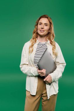 A woman with curly hair in casual attire smiles while holding a laptop, set against a bright green backdrop. clipart