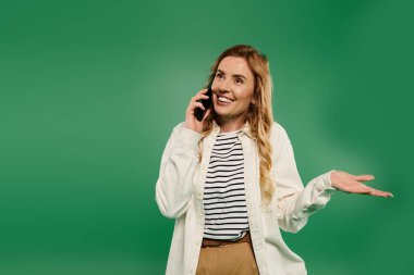 Kıvırcık saçlı neşeli bir kadın telefonuyla enerjik bir şekilde sohbet ediyor. Günlük kıyafetleriyle heyecanını dile getiriyor..
